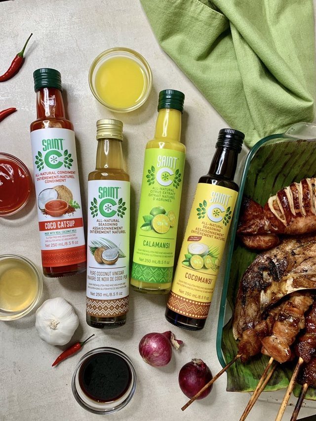 The four Saint C bottles beside chillies, garlic, onions and grilled meat on a banana leaf